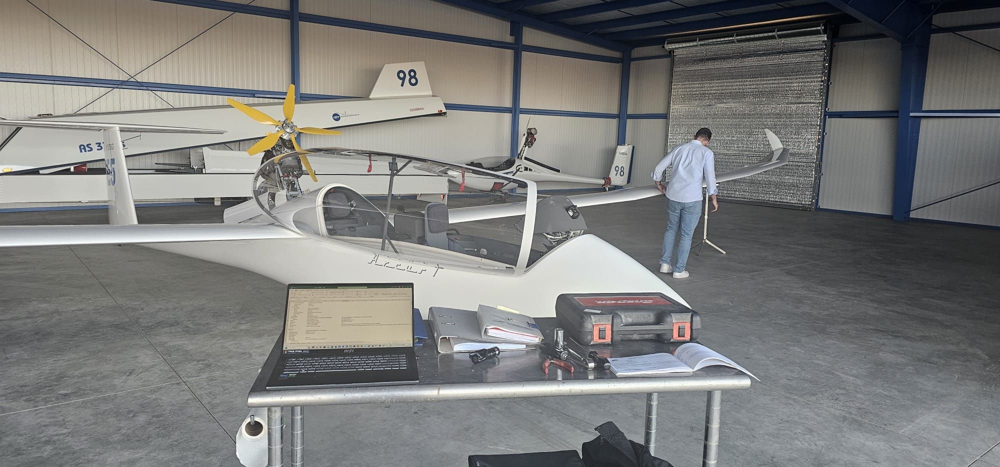 Der Arcus T in der Halle des Williams Soaring Centers – Logbücher, Laptop und Werkzeug auf dem Tisch bei der Begutachtung